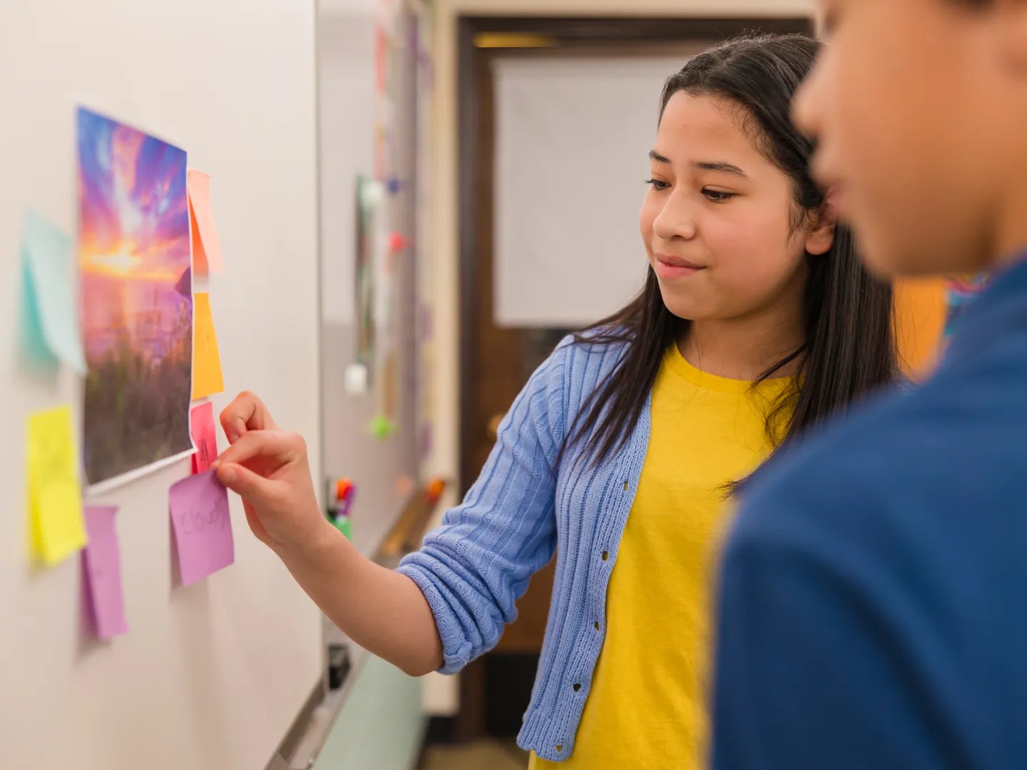A student places post it notes on a wall using a strategy learned from Ellevation
