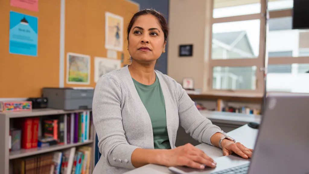 A teacher is typing on her computer at her desk.